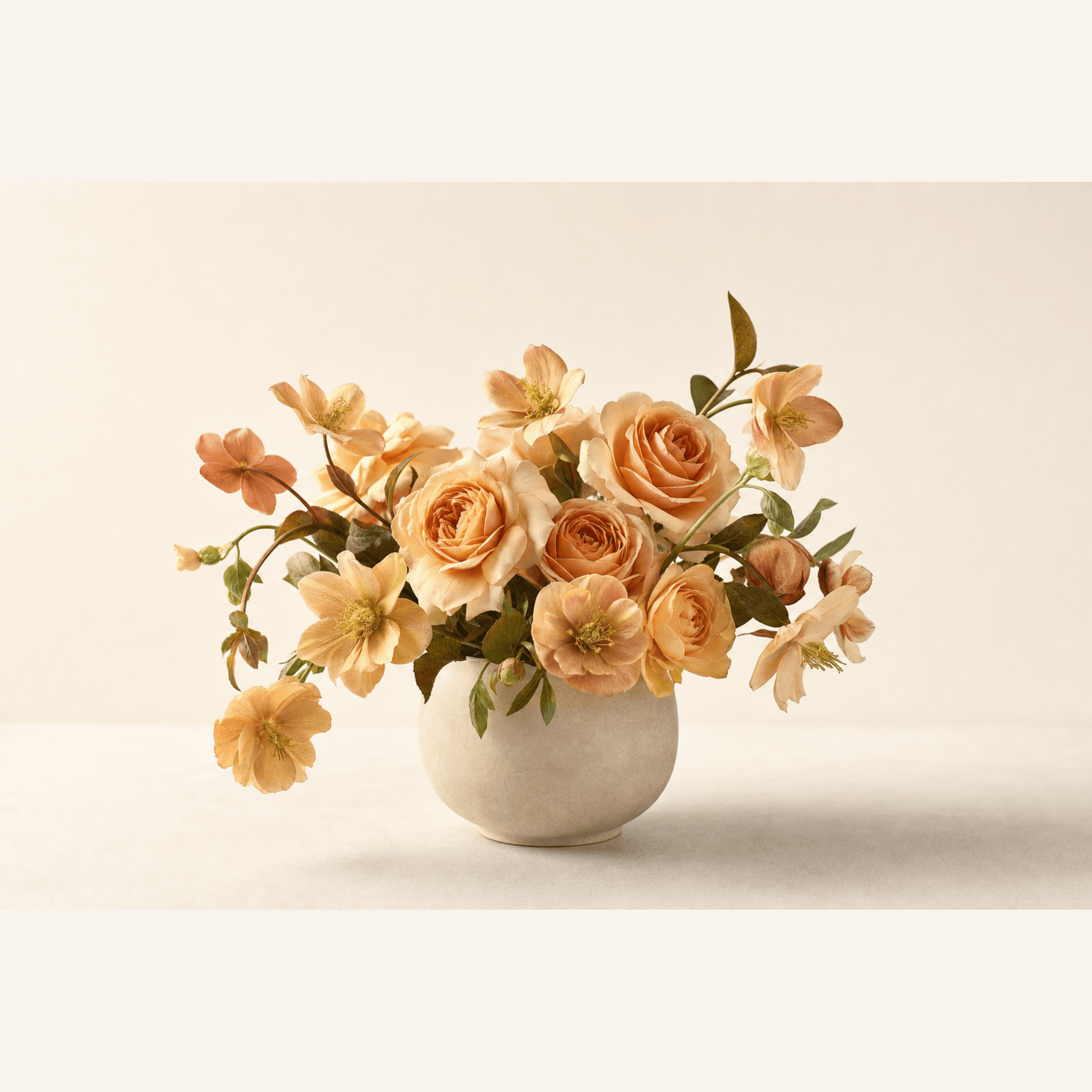 Peach garden roses and blush hellebores arranged in a round matte white ceramic bowl