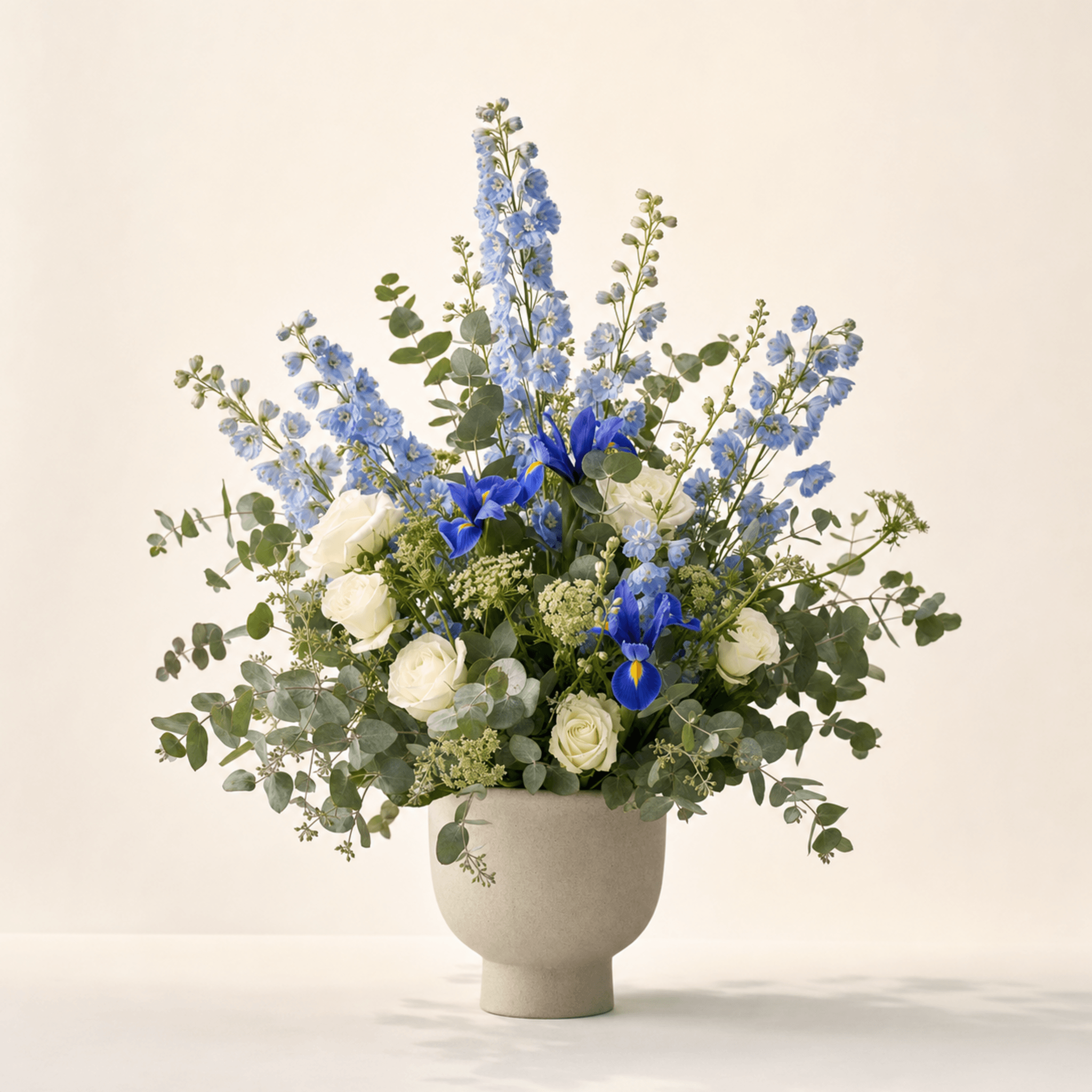 Blue delphiniums, purple irises, white roses and eucalyptus in a stone ceramic bowl vase