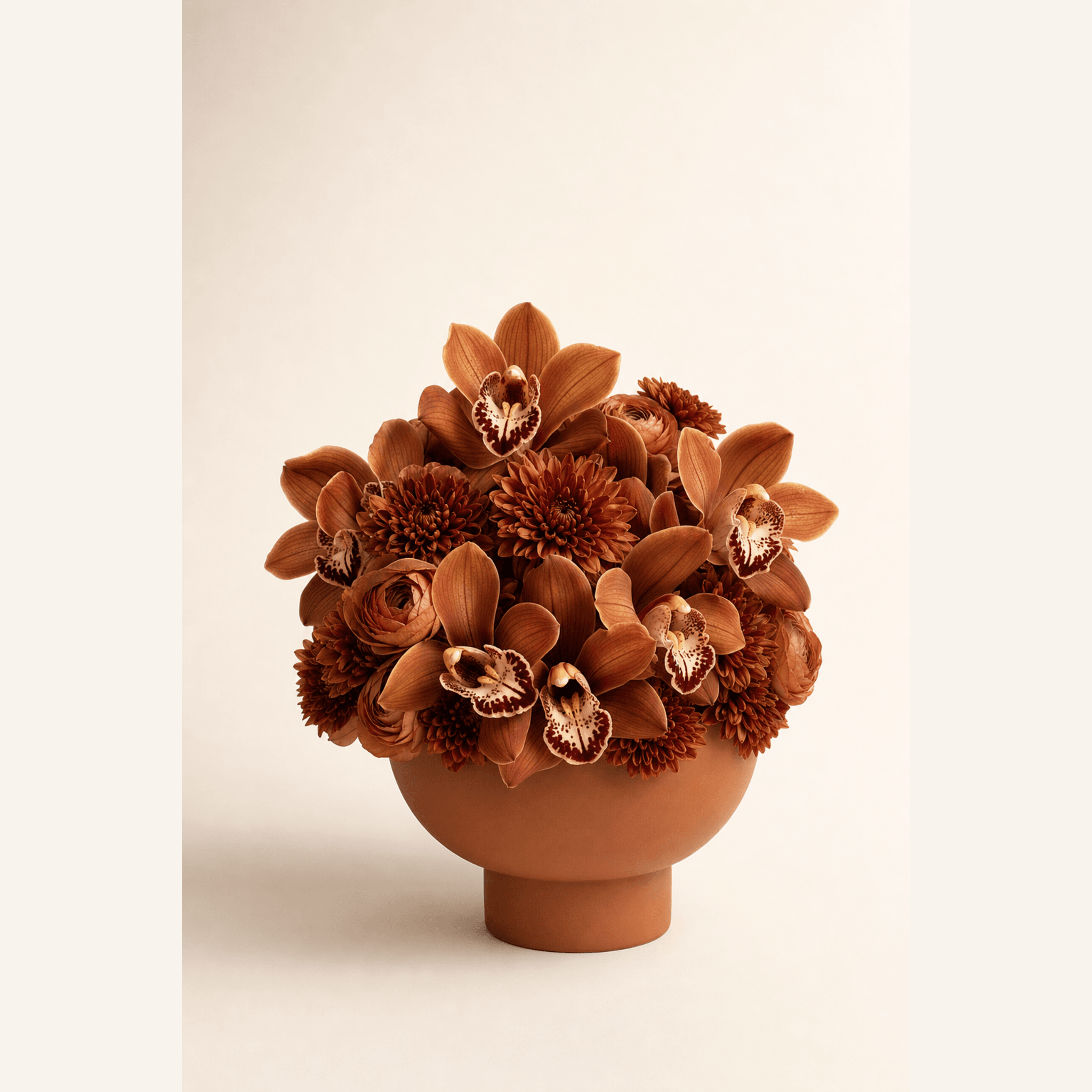 Rust and cream cymbidium orchids, burnt-orange ranunculus and bronze chrysanthemums in a terracotta bowl vase