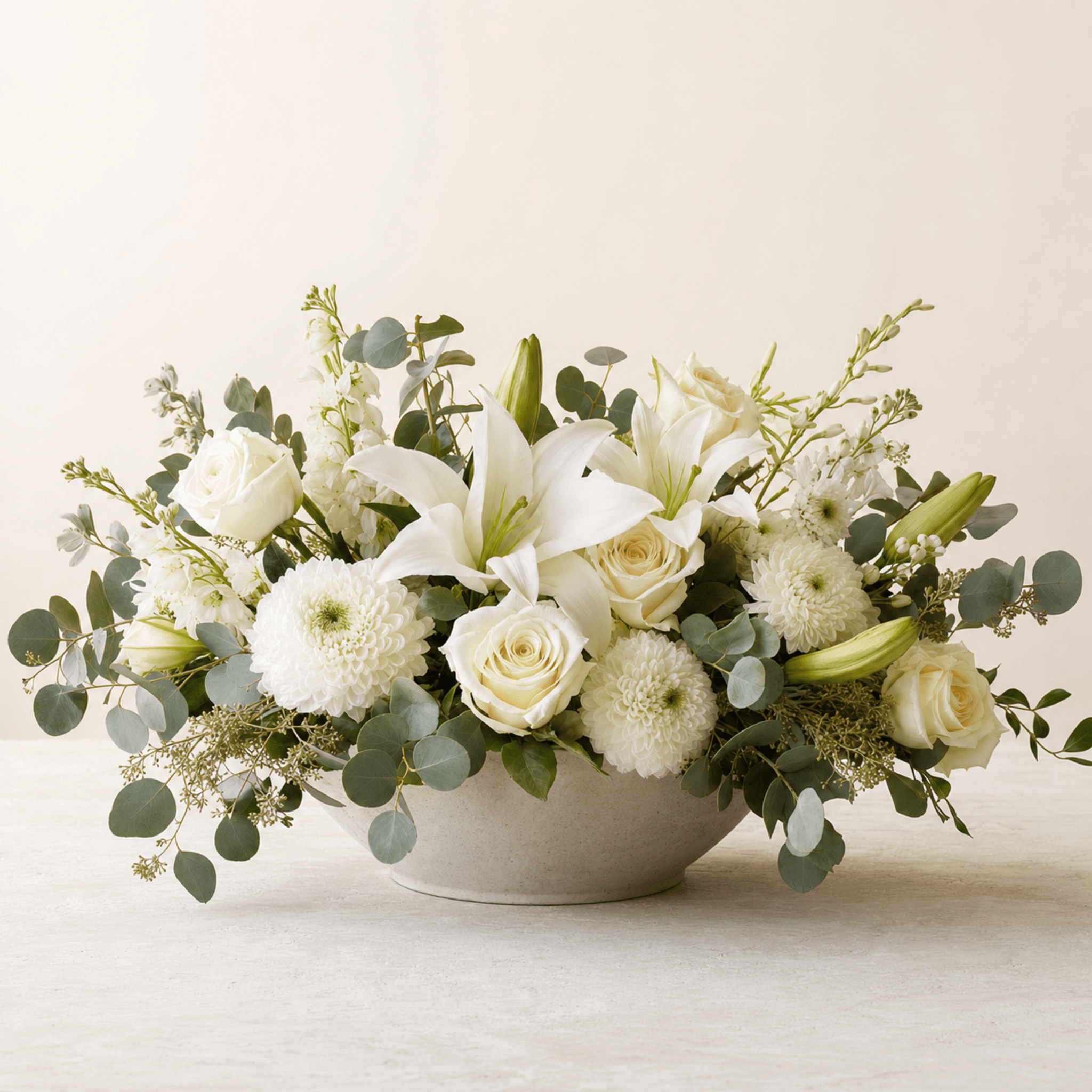White oriental lilies, cream roses, white chrysanthemums and eucalyptus in a low stone bowl