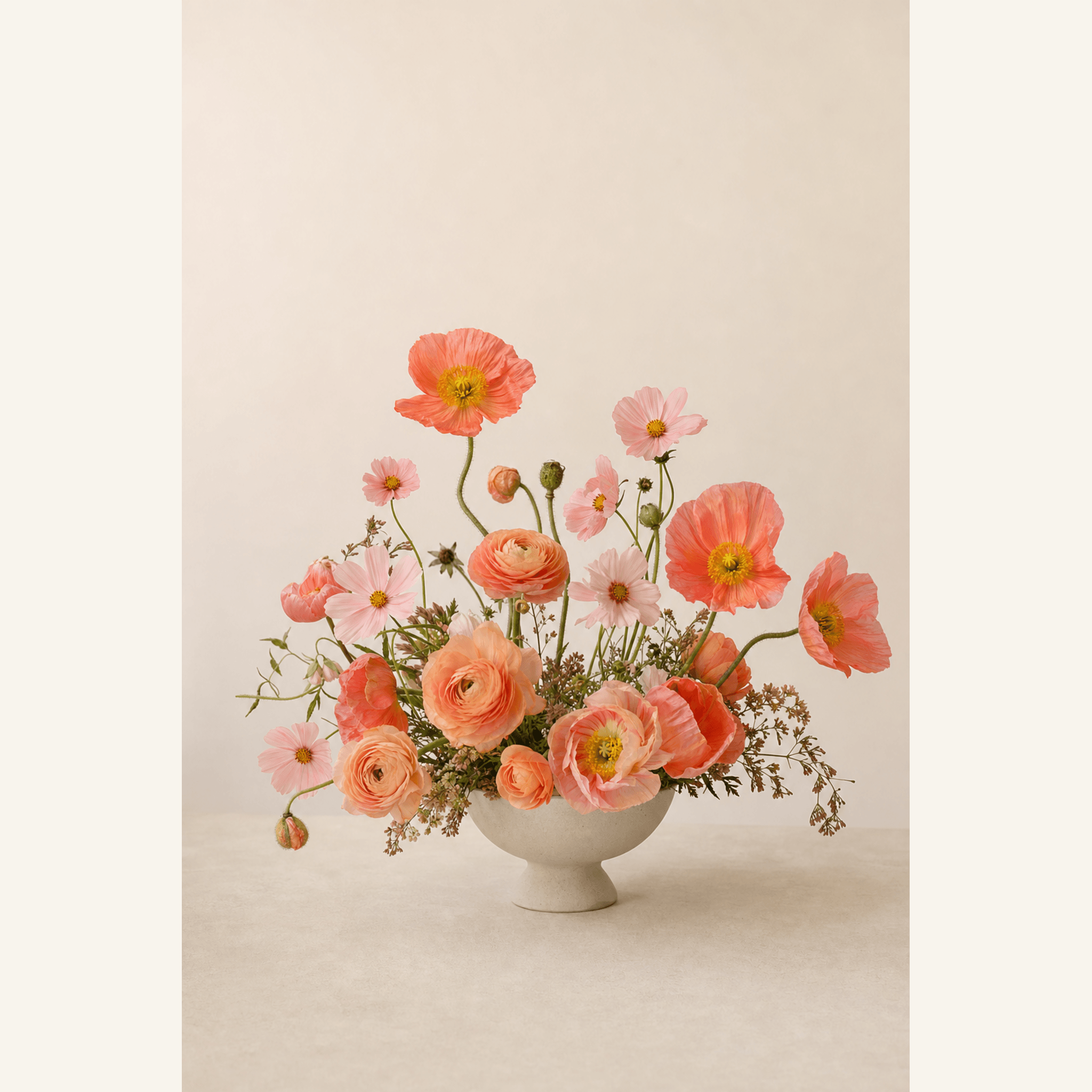 Coral poppies, peach ranunculus and blush cosmos arranged in a white ceramic footed bowl