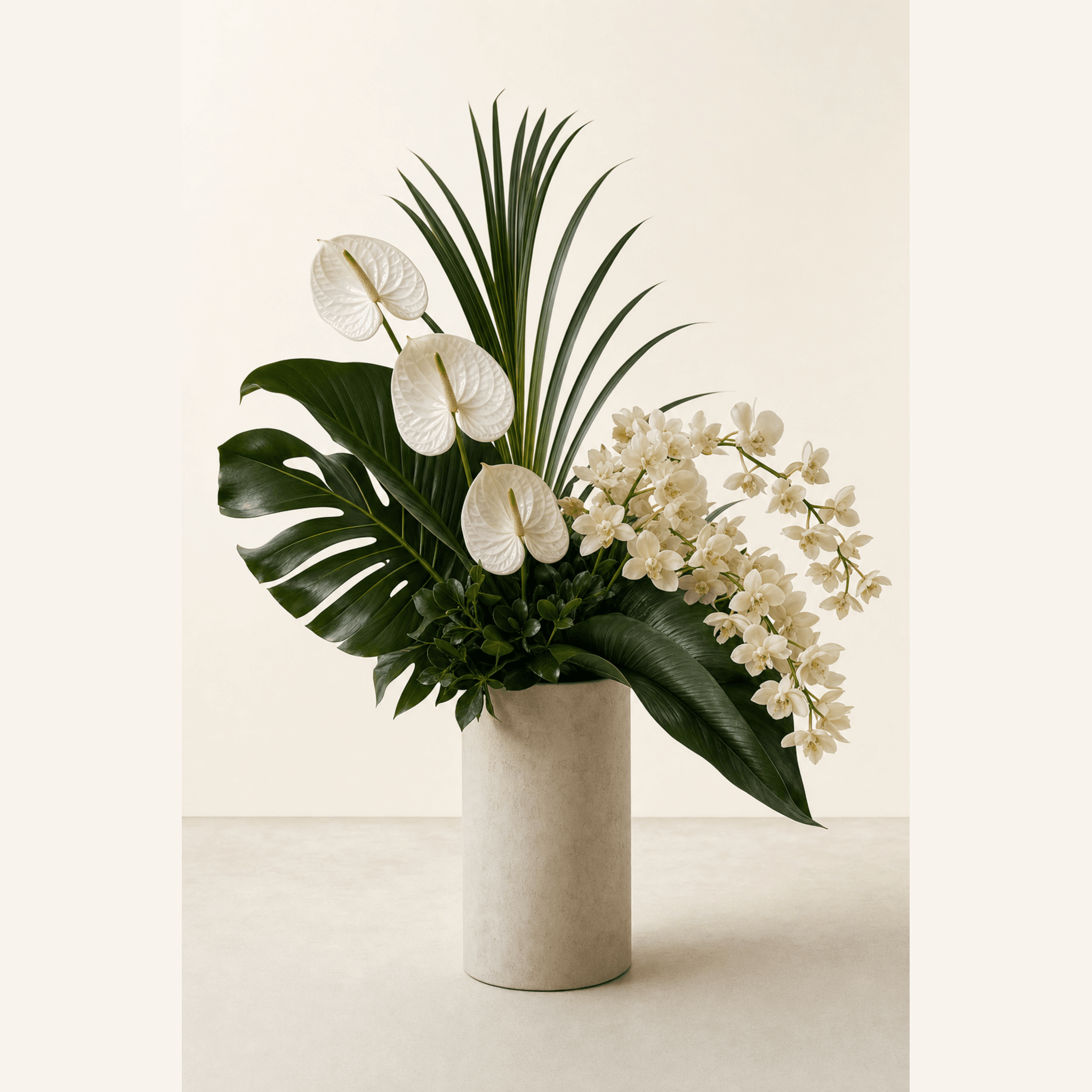 White anthuriums and cream orchids with tropical monstera and palm leaves in a cylindrical stone vase