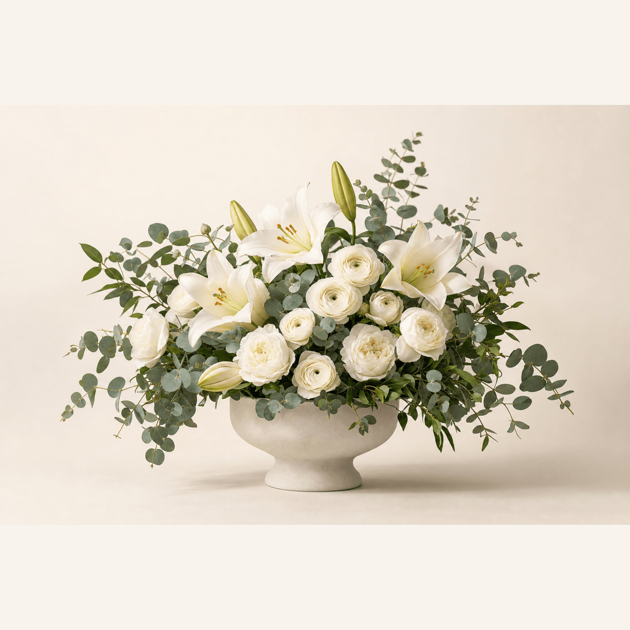 White oriental lilies, cream ranunculus, garden roses and eucalyptus in a stone pedestal bowl