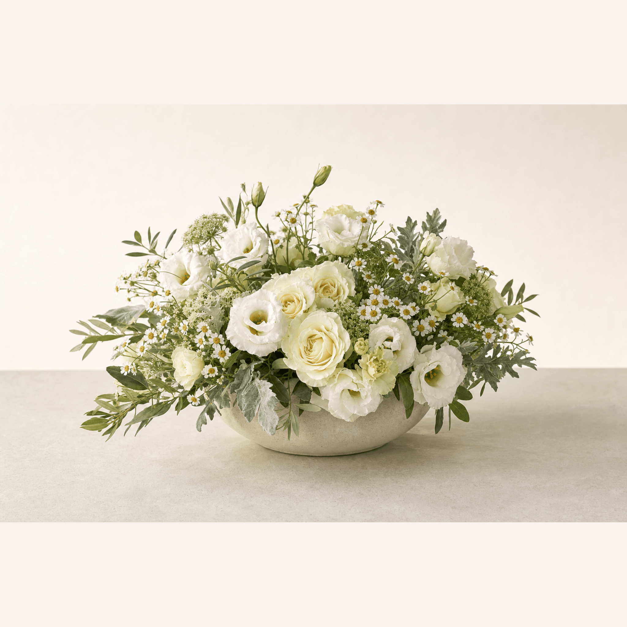 Cream roses, white lisianthus, chamomile and olive foliage arranged in a low stone bowl