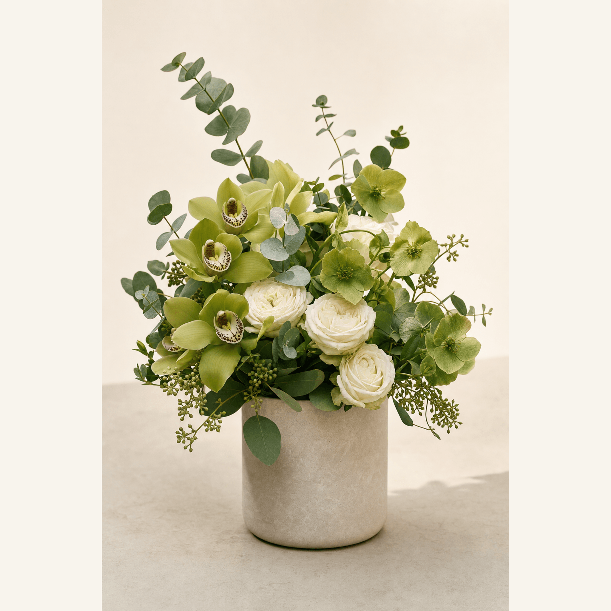 Green cymbidium orchids, white garden roses, hellebores and eucalyptus in a stone cylinder vase