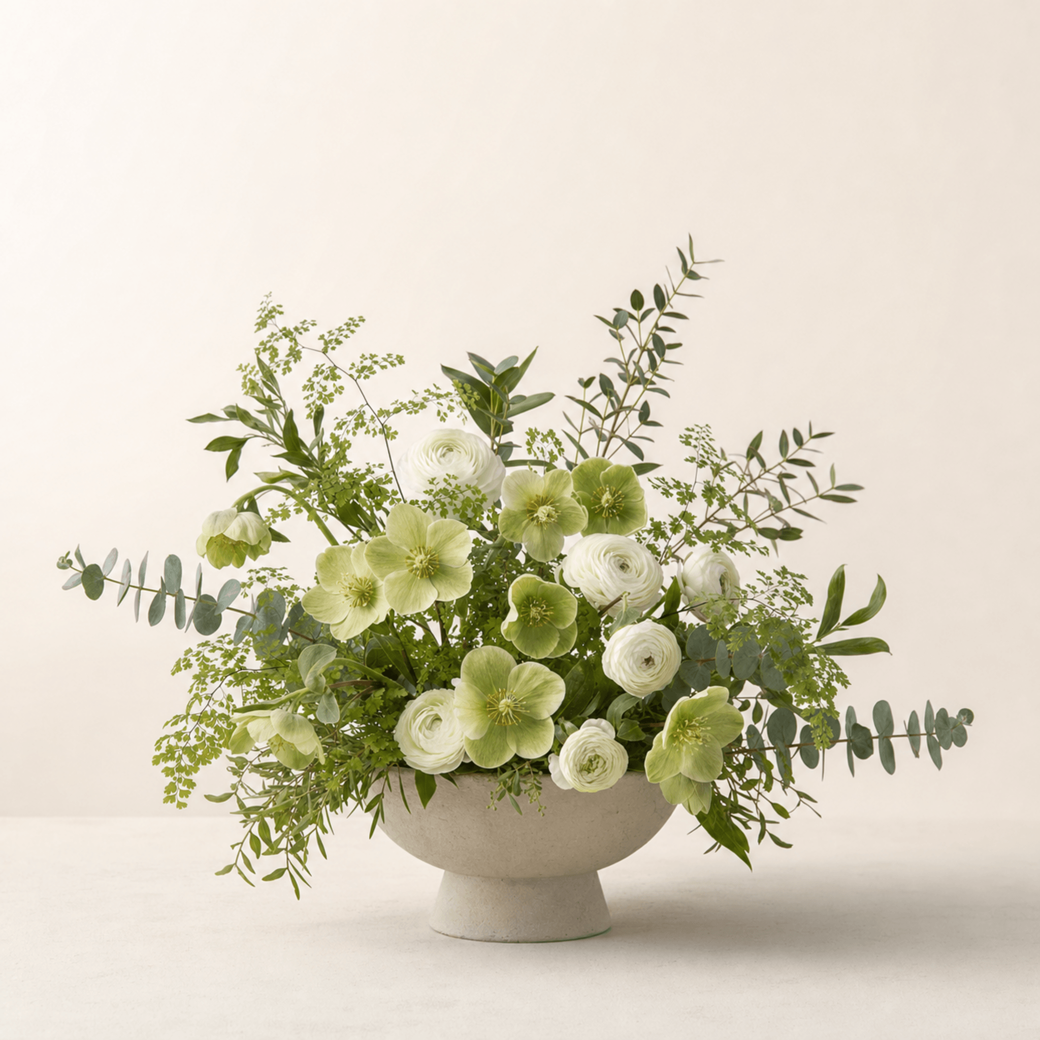 White ranunculus and green hellebores with eucalyptus and maidenhair fern in a stone pedestal bowl