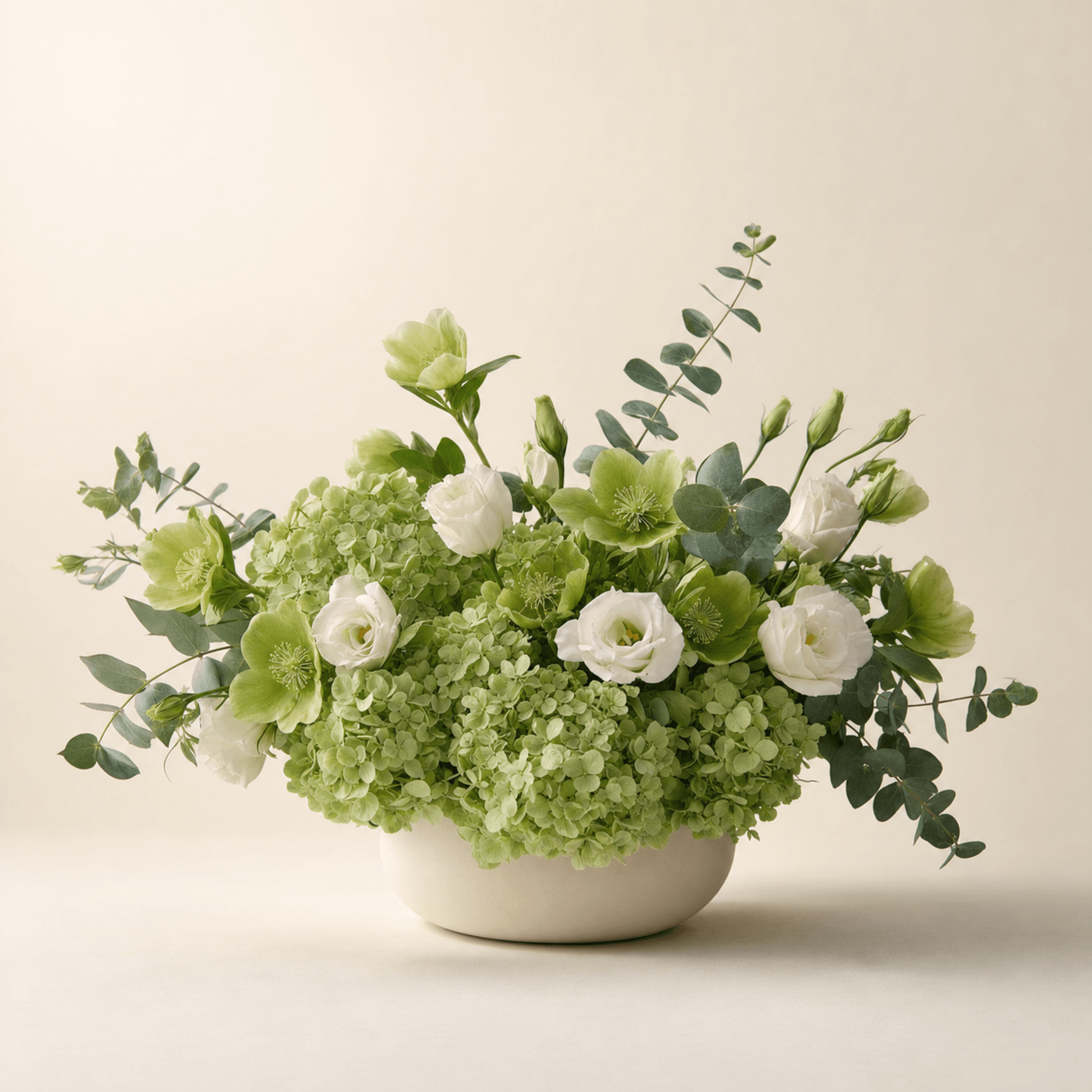 Green hydrangeas, white lisianthus, hellebores and eucalyptus arranged in a cream ceramic bowl