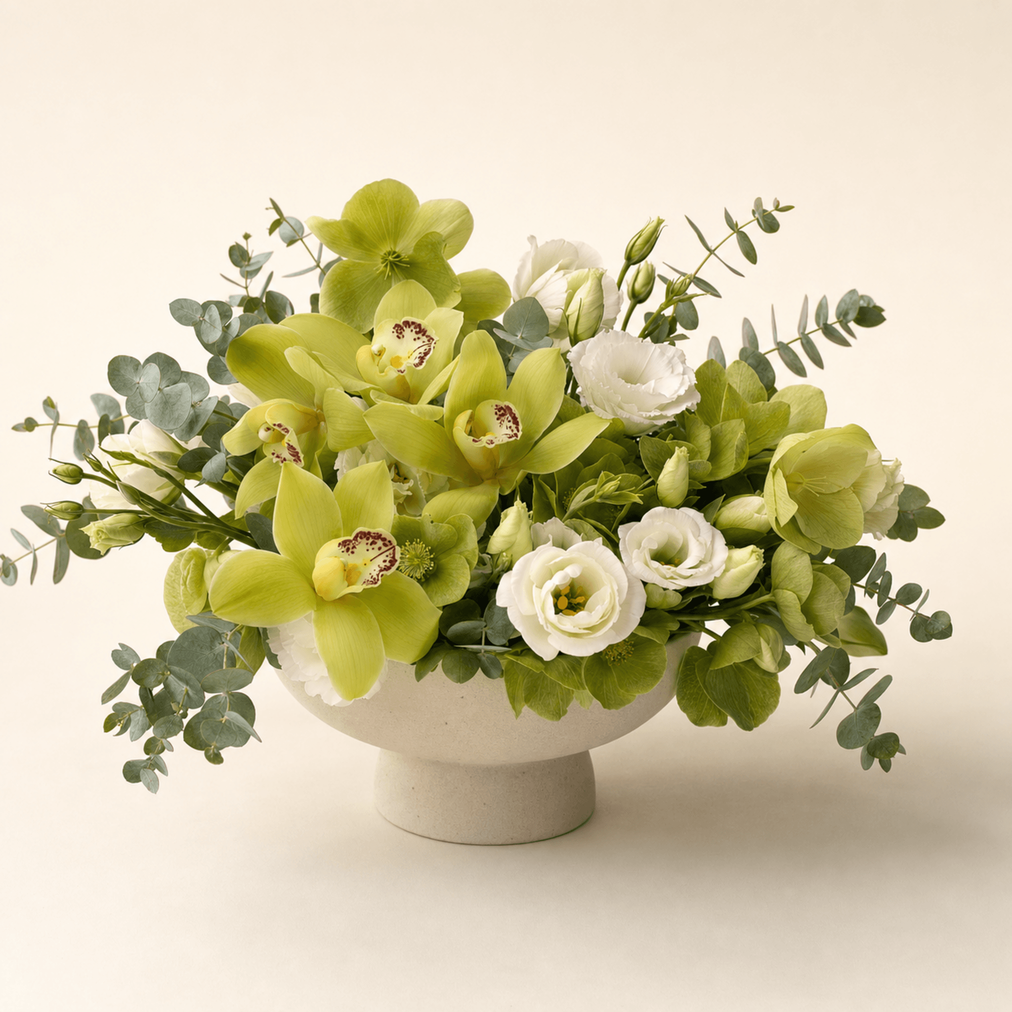Green cymbidium orchids, white lisianthus and hellebores in a cream ceramic footed bowl