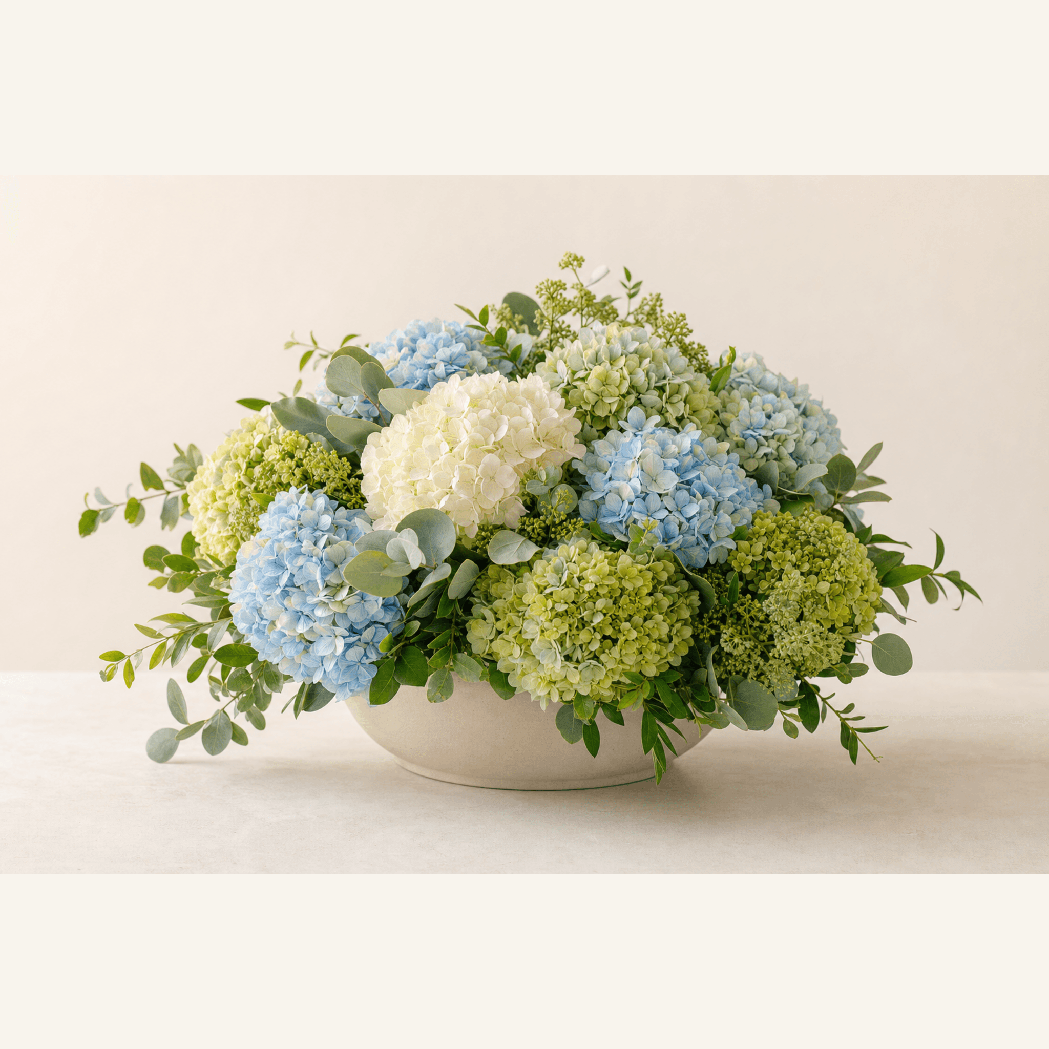 Blue, white and green hydrangeas with eucalyptus and viburnum in a white ceramic bowl