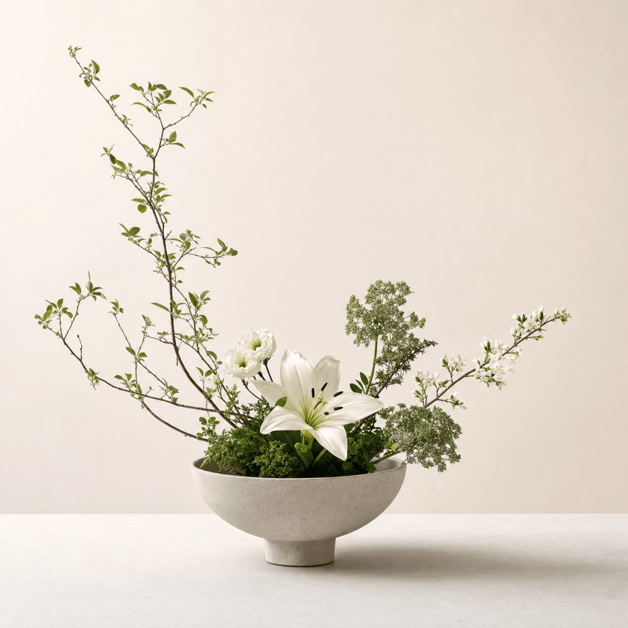 White lily and ranunculus with leafy branches and blossom in a stone pedestal bowl