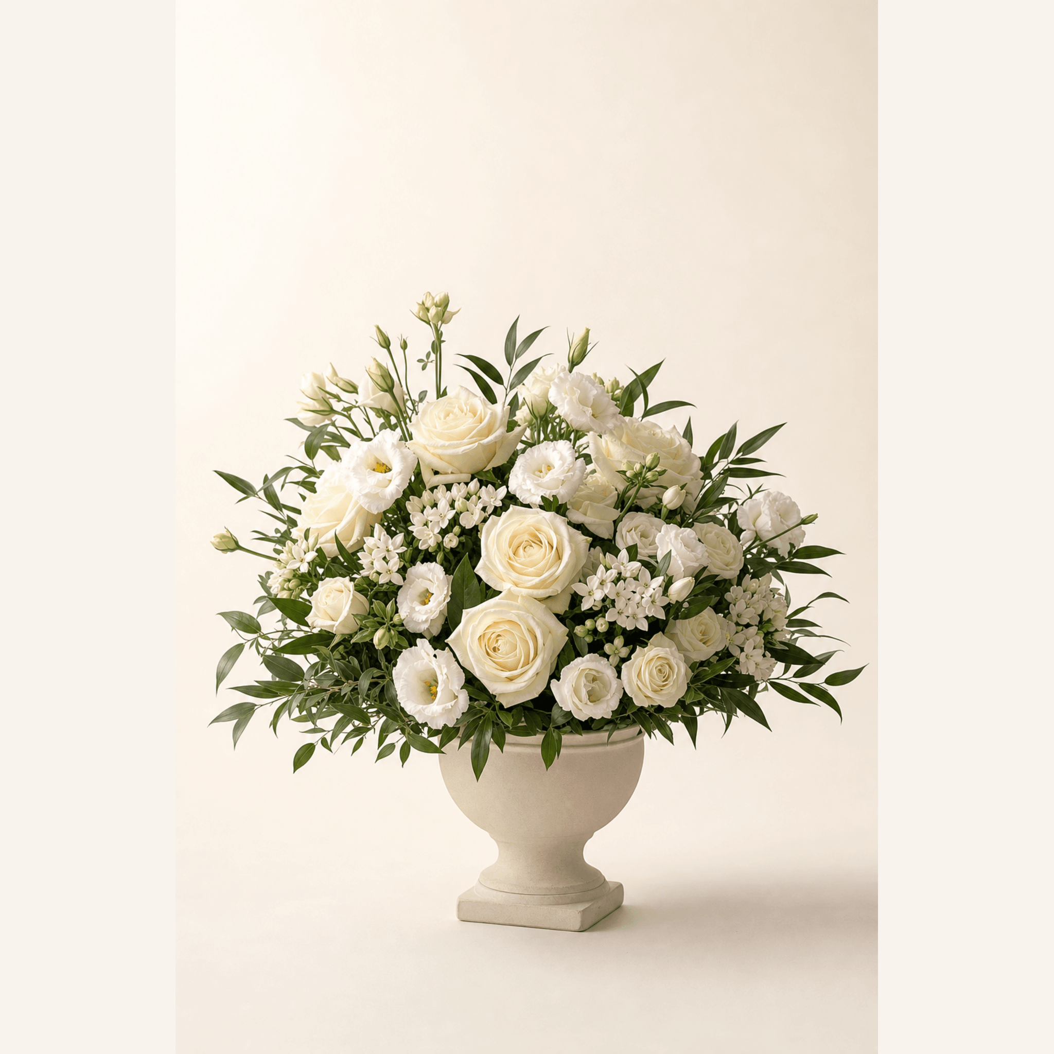 Cream roses, white lisianthus and delicate white star flowers arranged in a stone urn vase