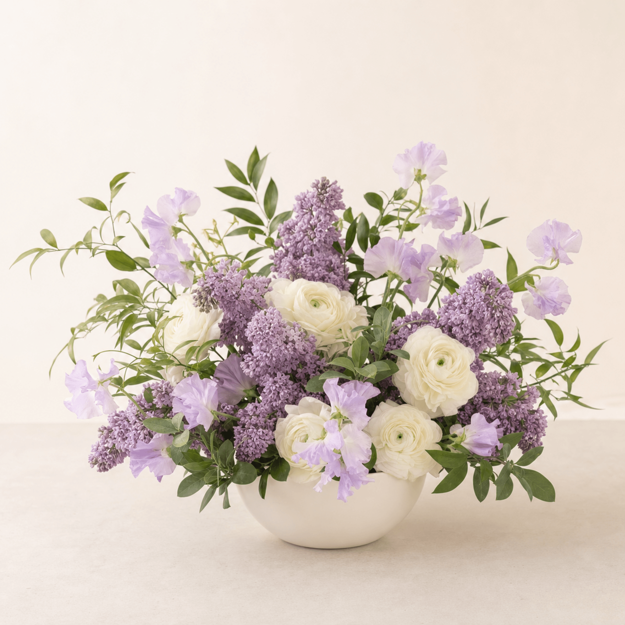 Purple lilac, white ranunculus and lavender sweet peas arranged in a white ceramic bowl