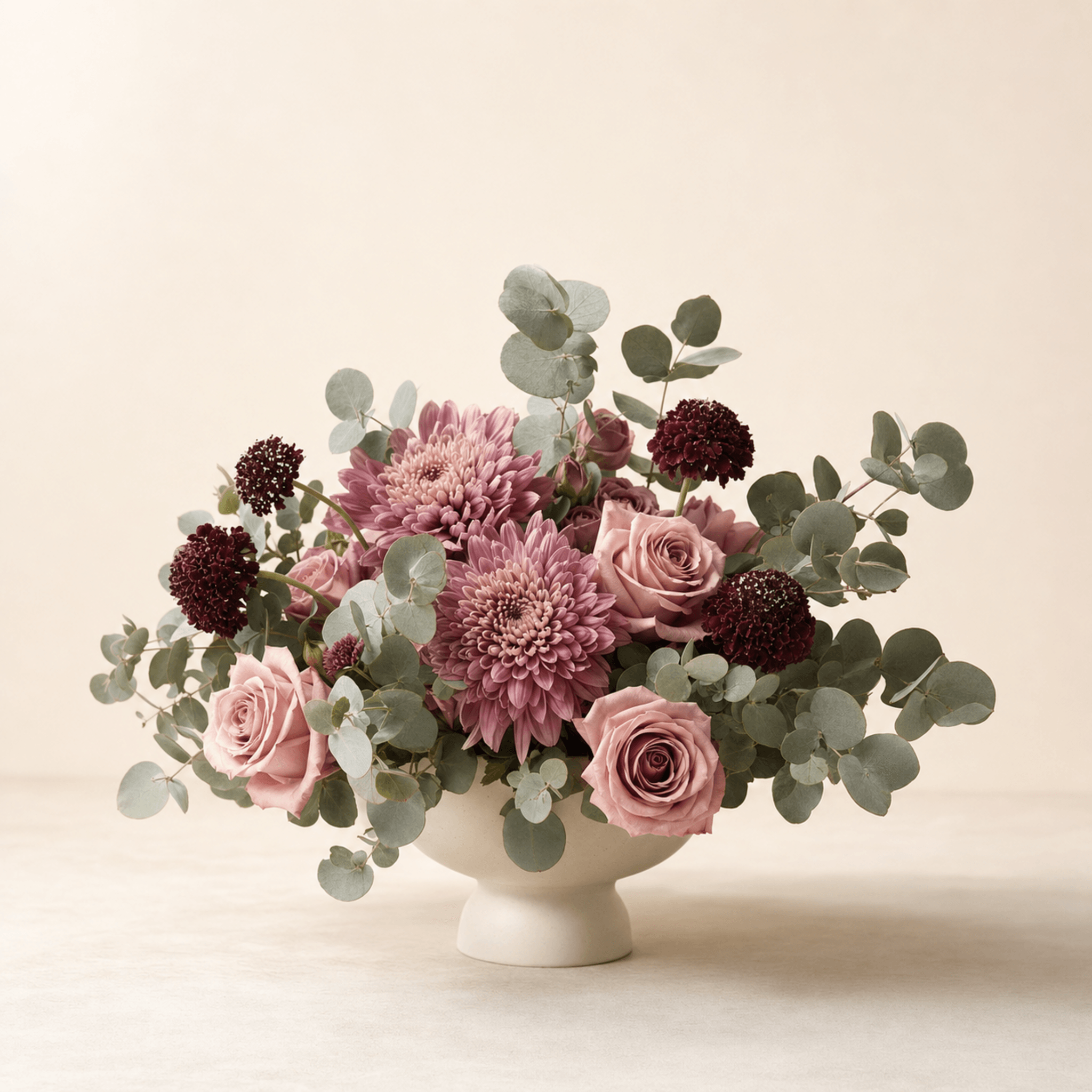 Mauve chrysanthemums, blush roses and burgundy scabiosa in a cream ceramic footed bowl with silver dollar eucalyptus