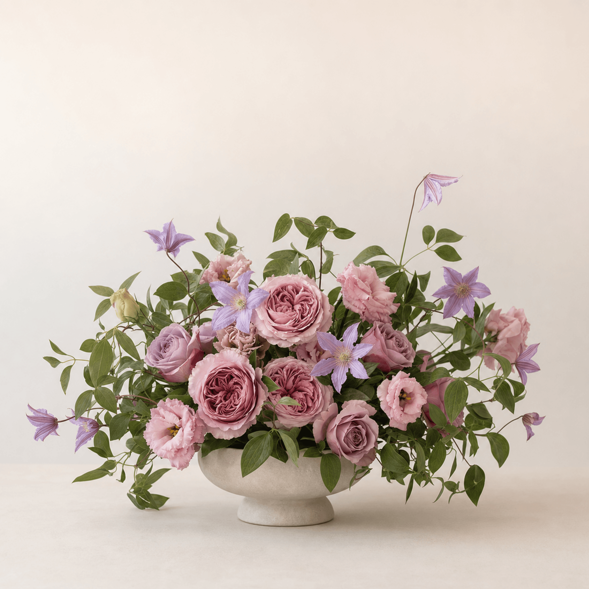 Pink garden roses, lisianthus, mauve roses and purple clematis in a stone footed bowl
