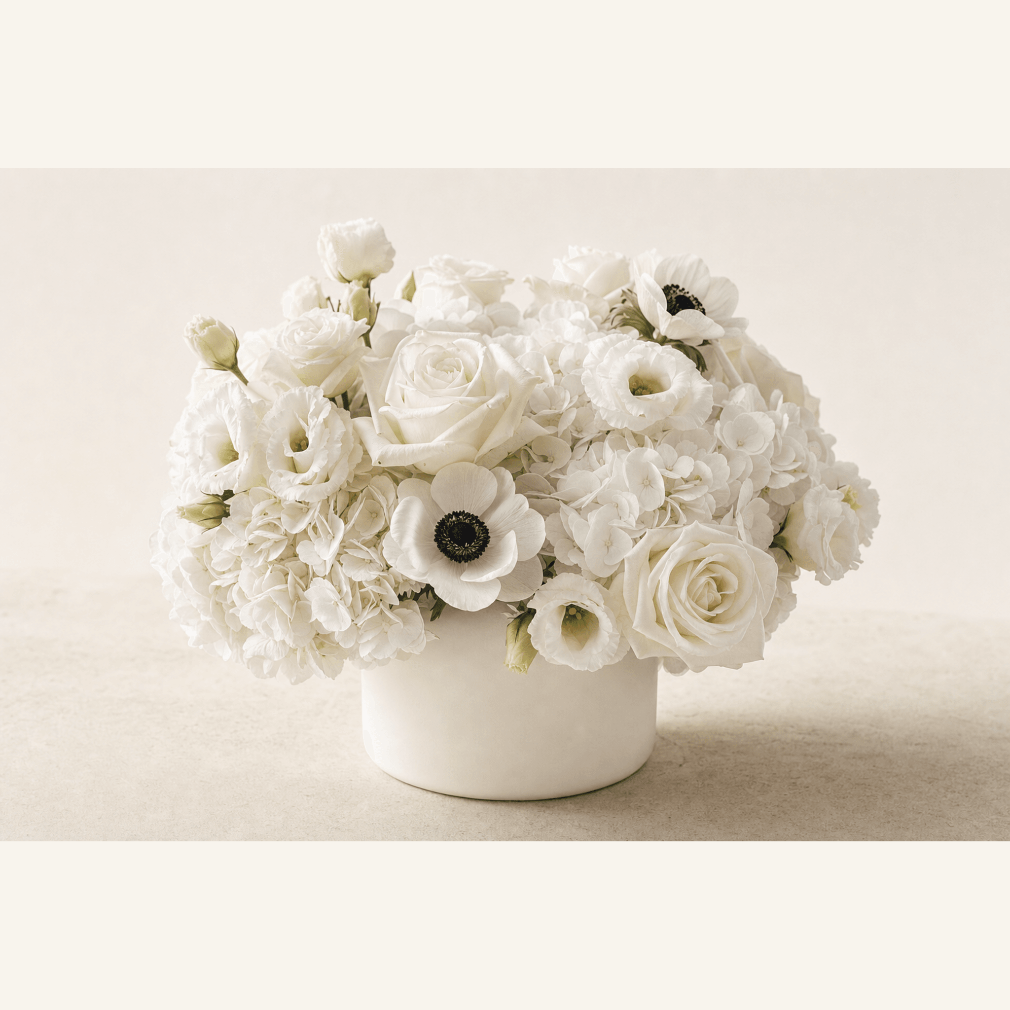 White hydrangeas, roses, lisianthus and anemones arranged in a round white ceramic bowl