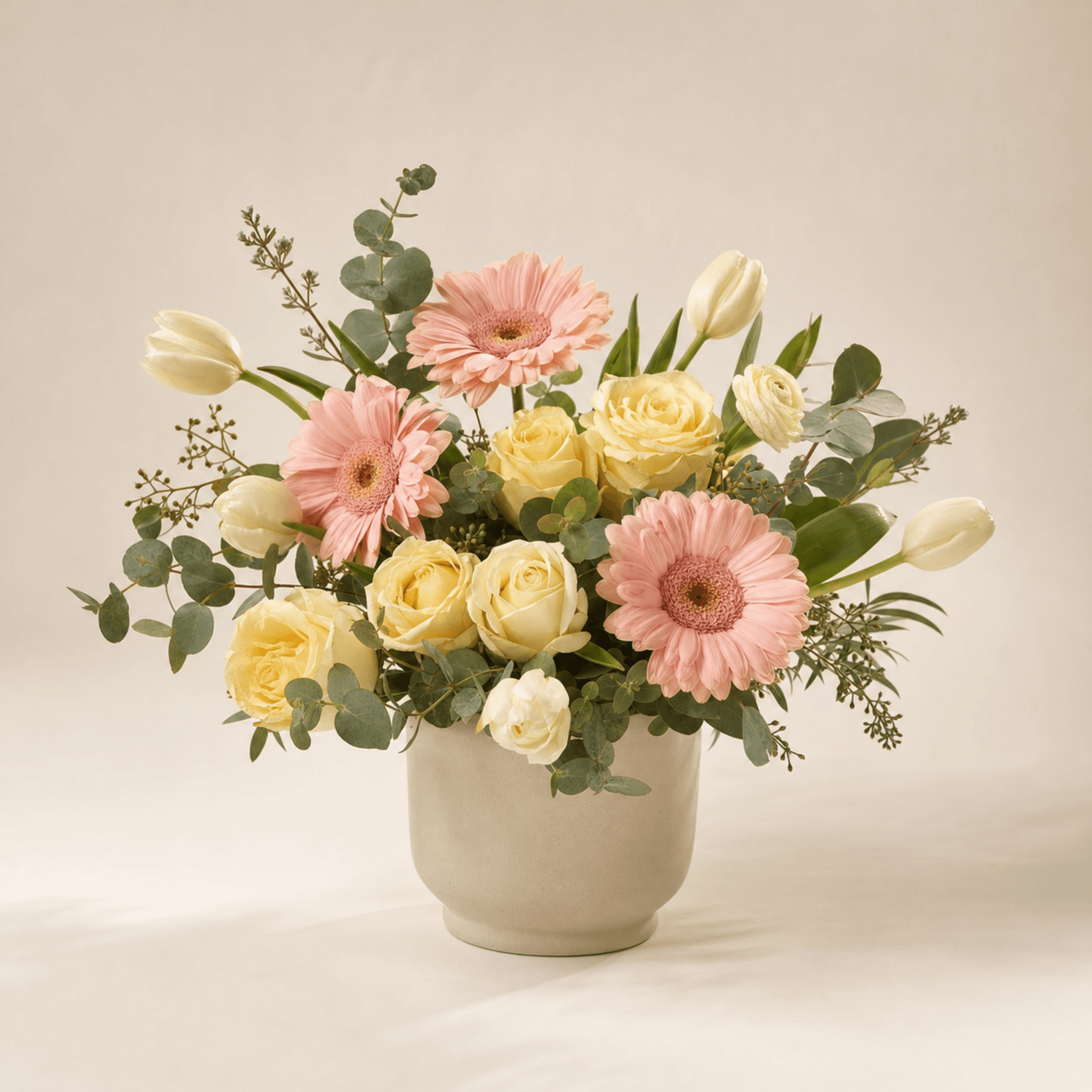 Pink gerberas, cream roses and white tulips with eucalyptus in a stone ceramic vase