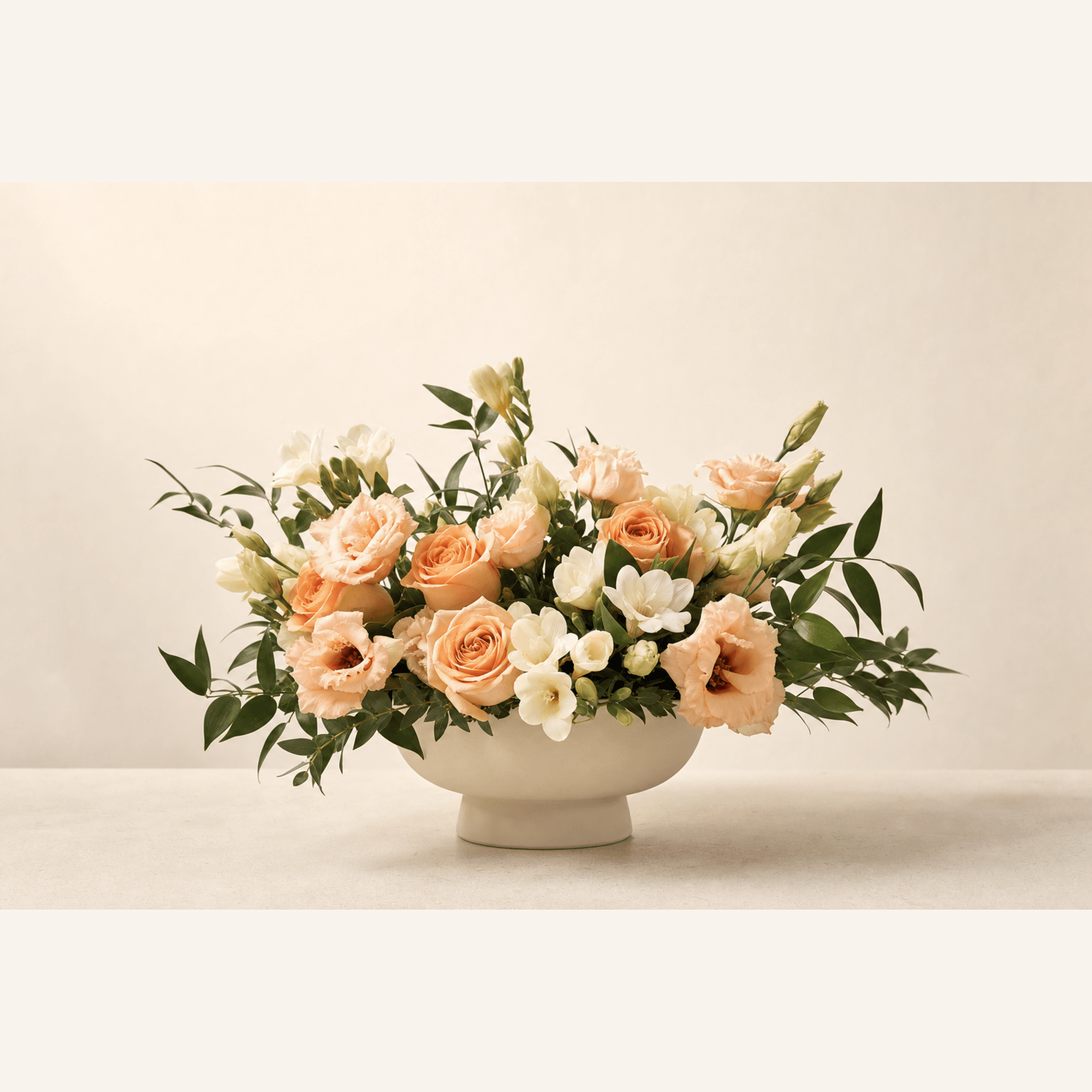 Peach roses, blush lisianthus and white freesia arranged in a wide cream ceramic footed bowl