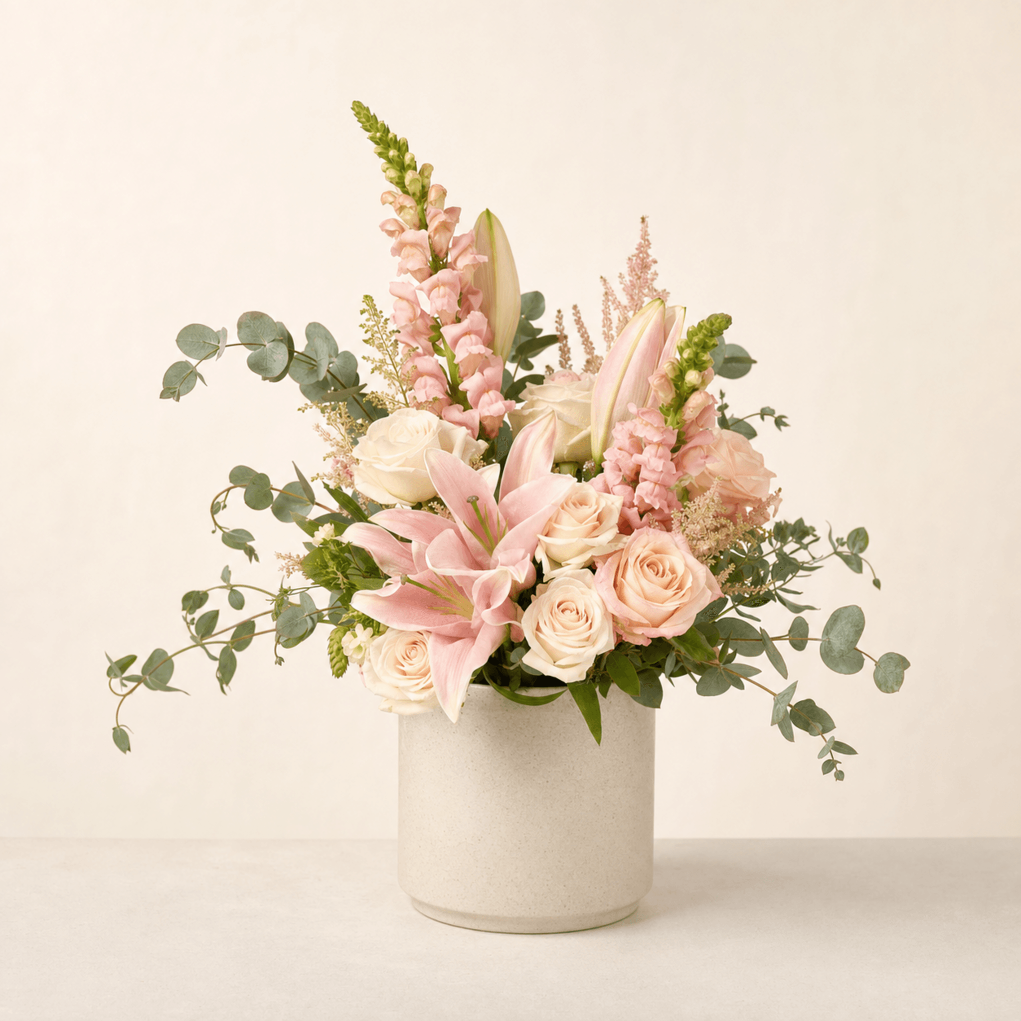 Pink lilies, blush and white roses, pink snapdragons, astilbe and eucalyptus in a white ceramic vase