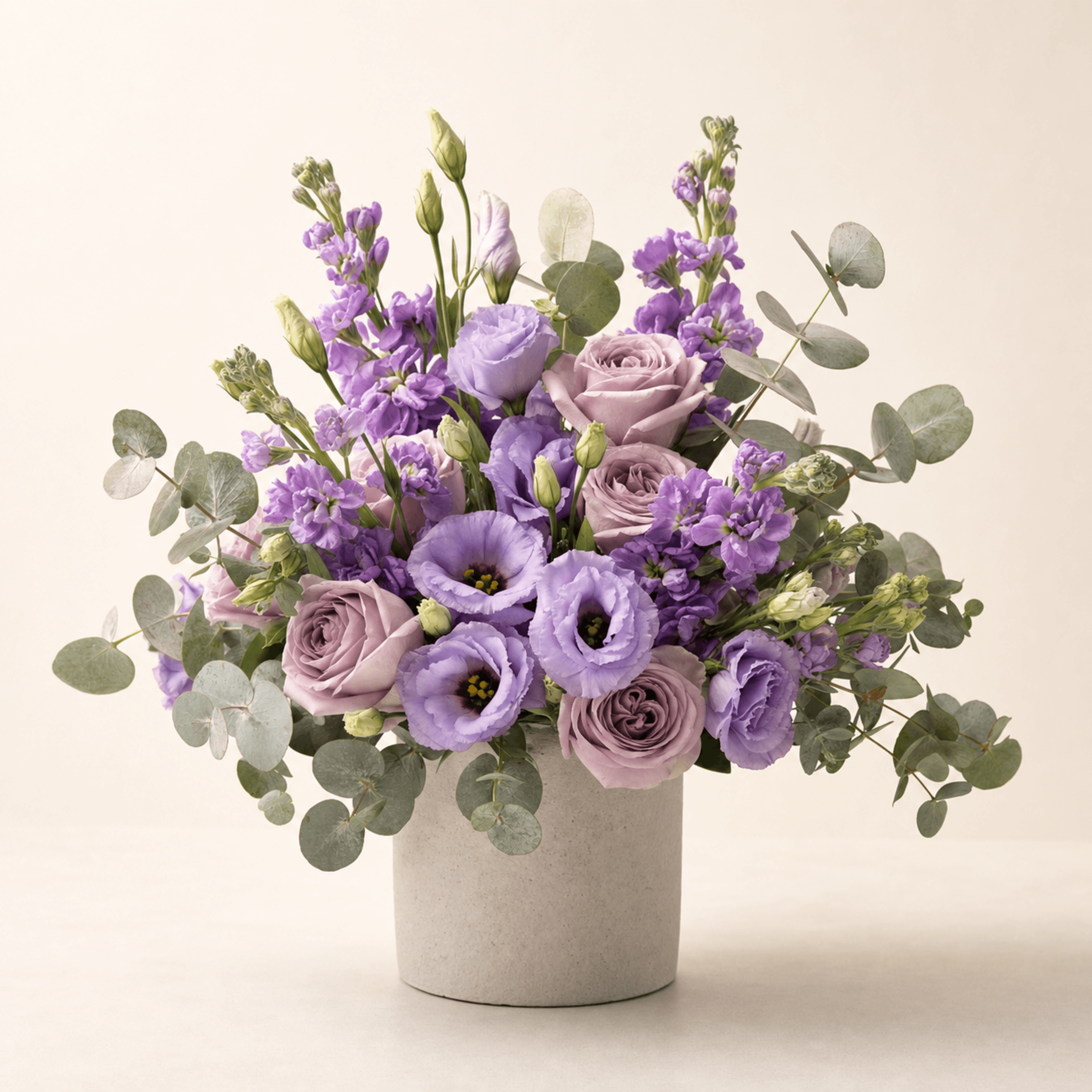 Purple lisianthus, lavender roses, violet stock and silver eucalyptus arranged in a stone cylinder vase