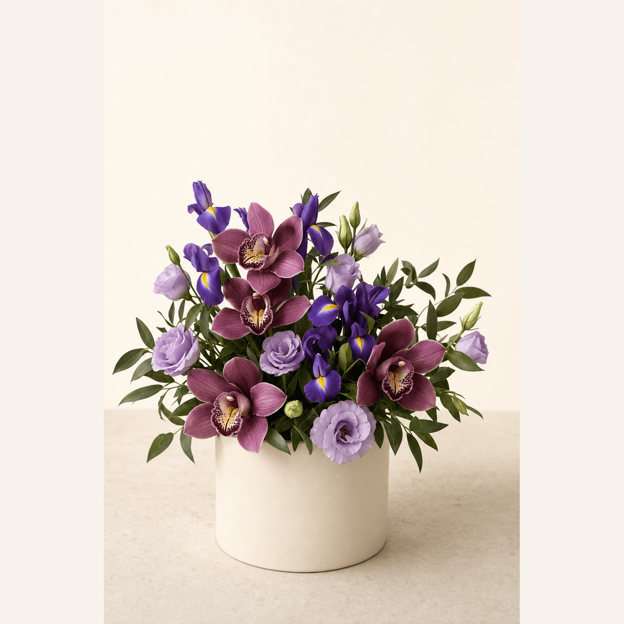Deep burgundy cymbidium orchids, purple iris and lavender lisianthus arranged in a white ceramic pot