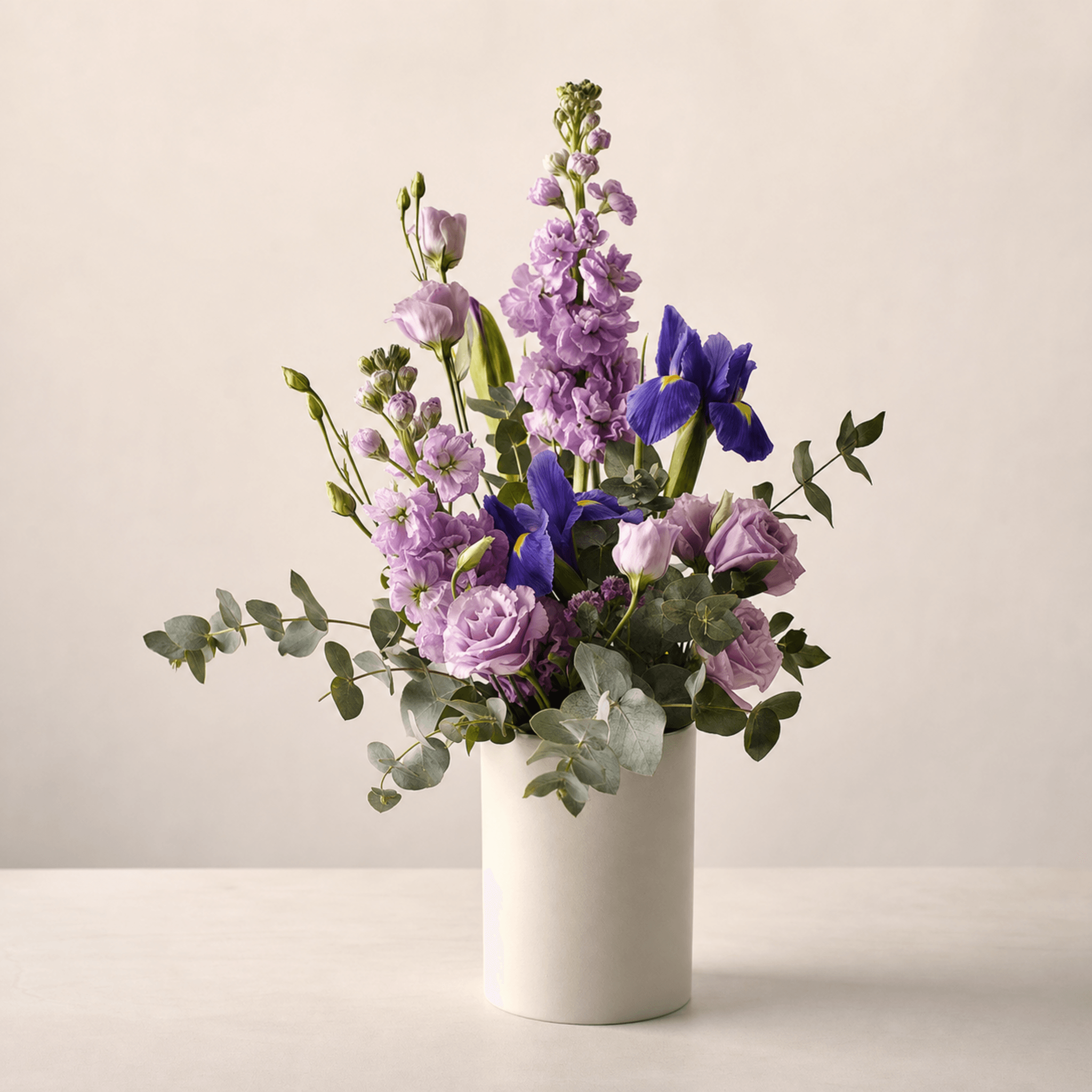 Lavender stock, purple irises, lilac lisianthus and roses in a white ceramic vase with eucalyptus