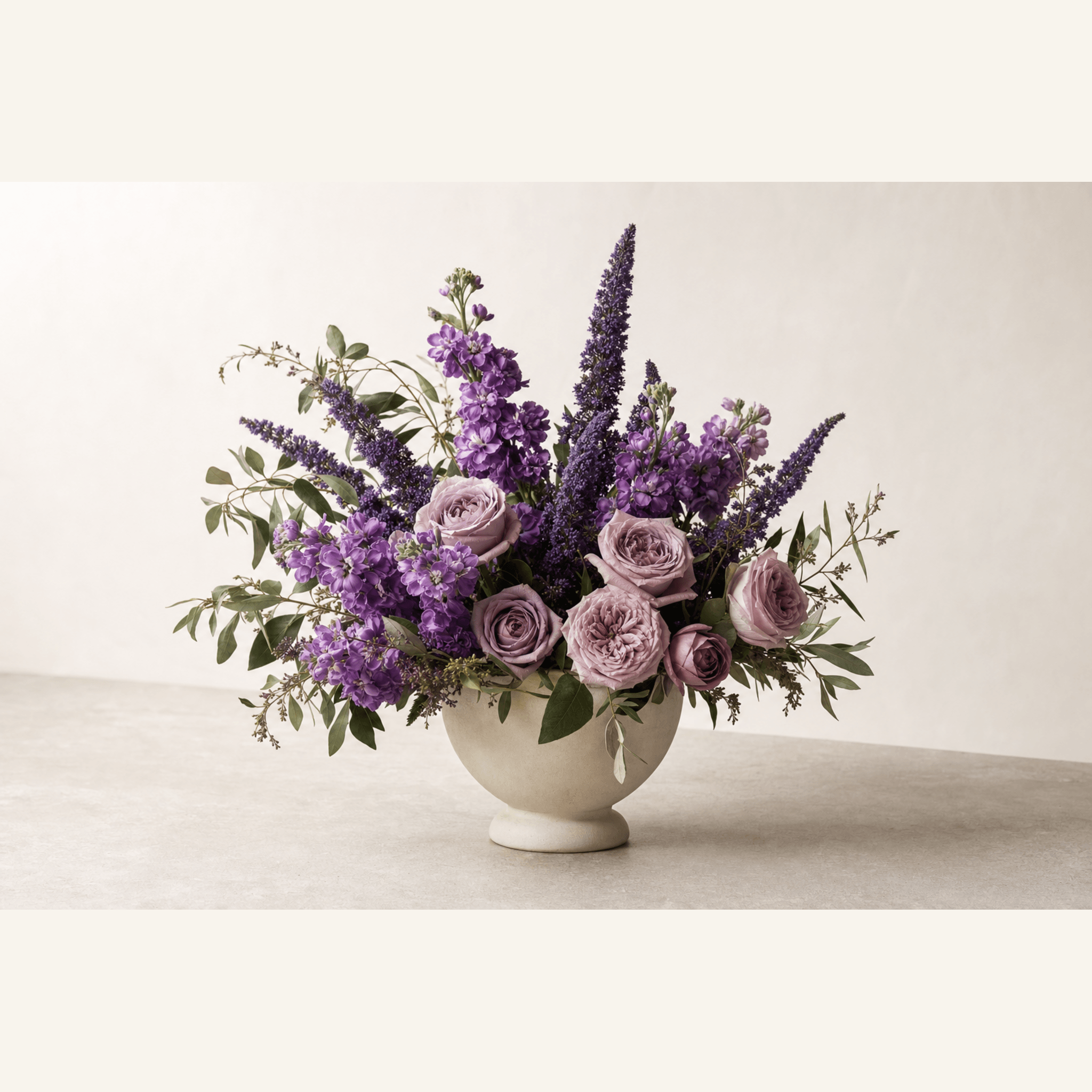Purple stock, lavender roses, violet salvia and eucalyptus in a cream ceramic footed bowl