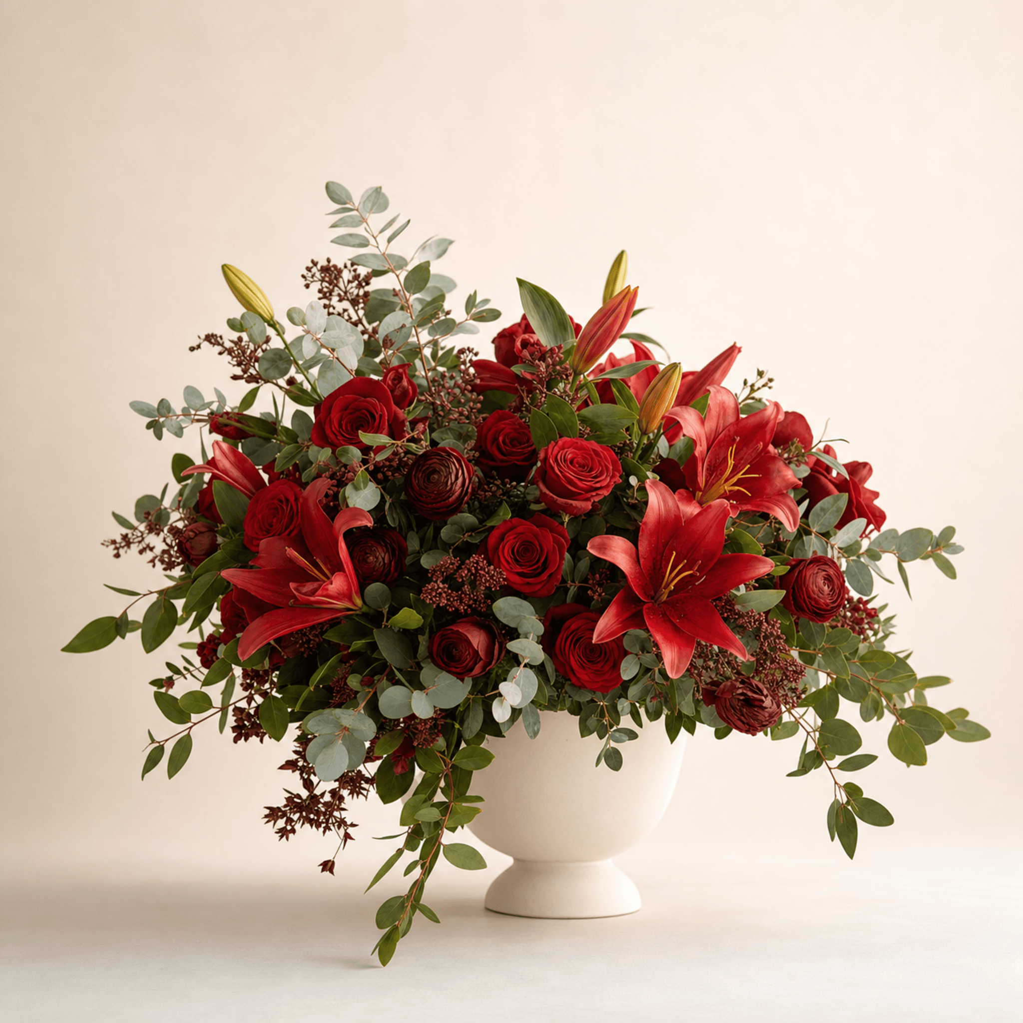 Red roses, crimson lilies and dark ranunculus with eucalyptus in a white footed bowl