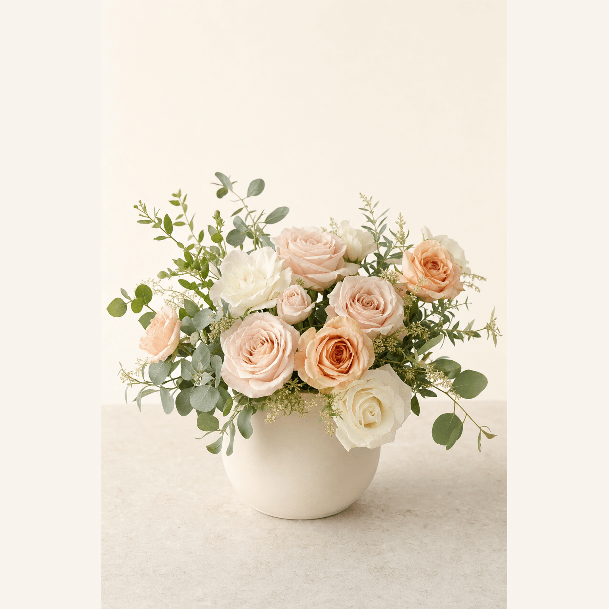 Blush pink, peach, and white roses with eucalyptus in a round white ceramic vase