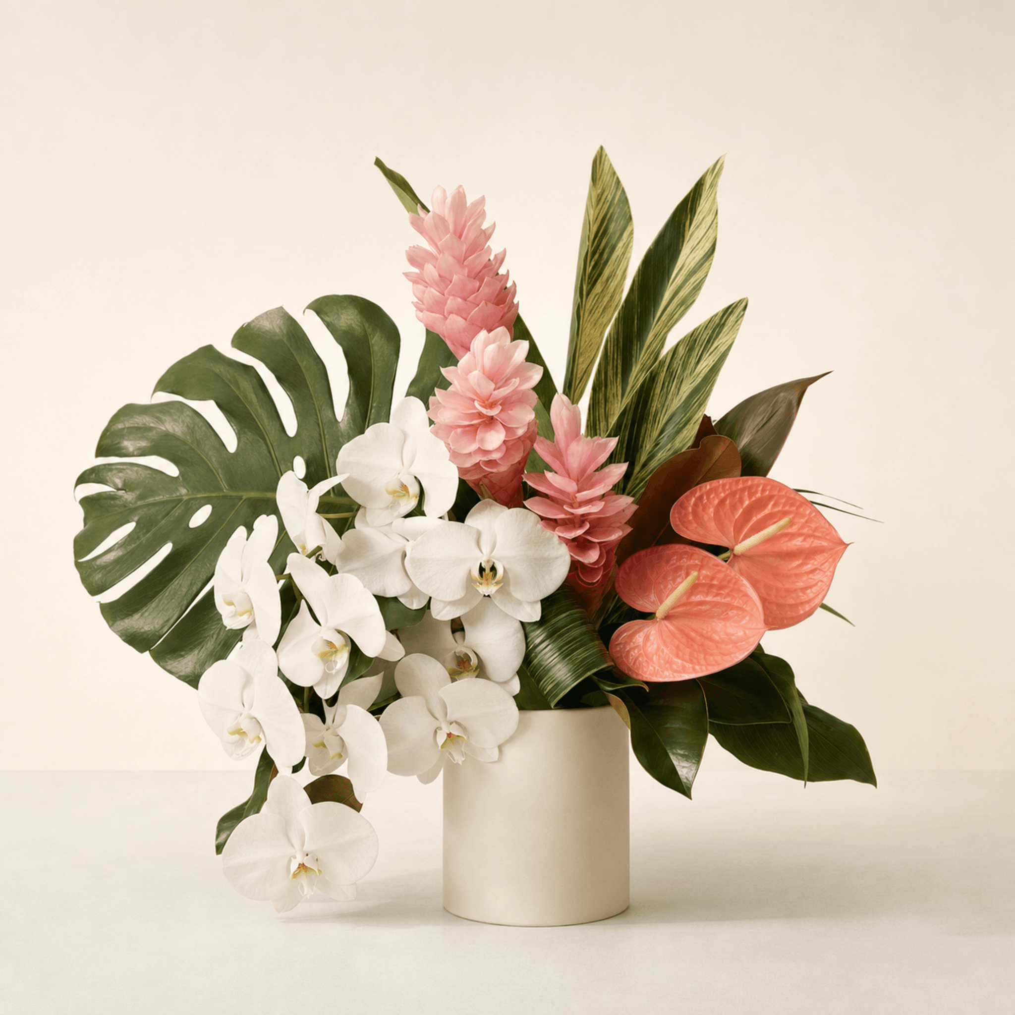 White phalaenopsis orchids, pink ginger, coral anthuriums and monstera leaves in a cream ceramic vase