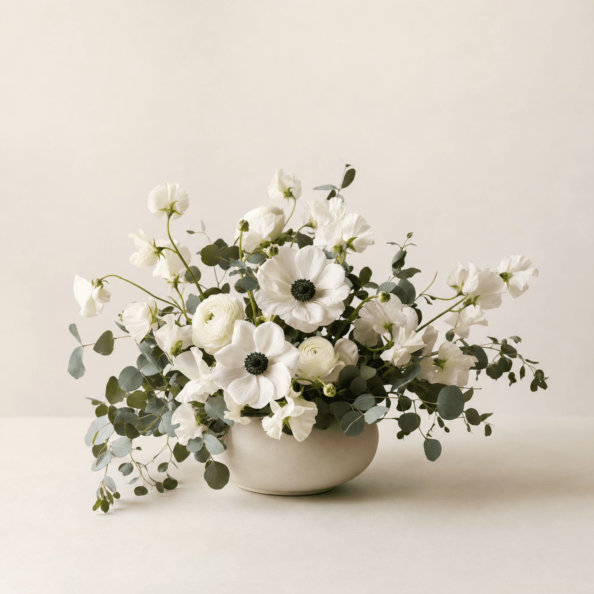 White anemones, ranunculus and sweet peas with eucalyptus in a round cream ceramic bowl