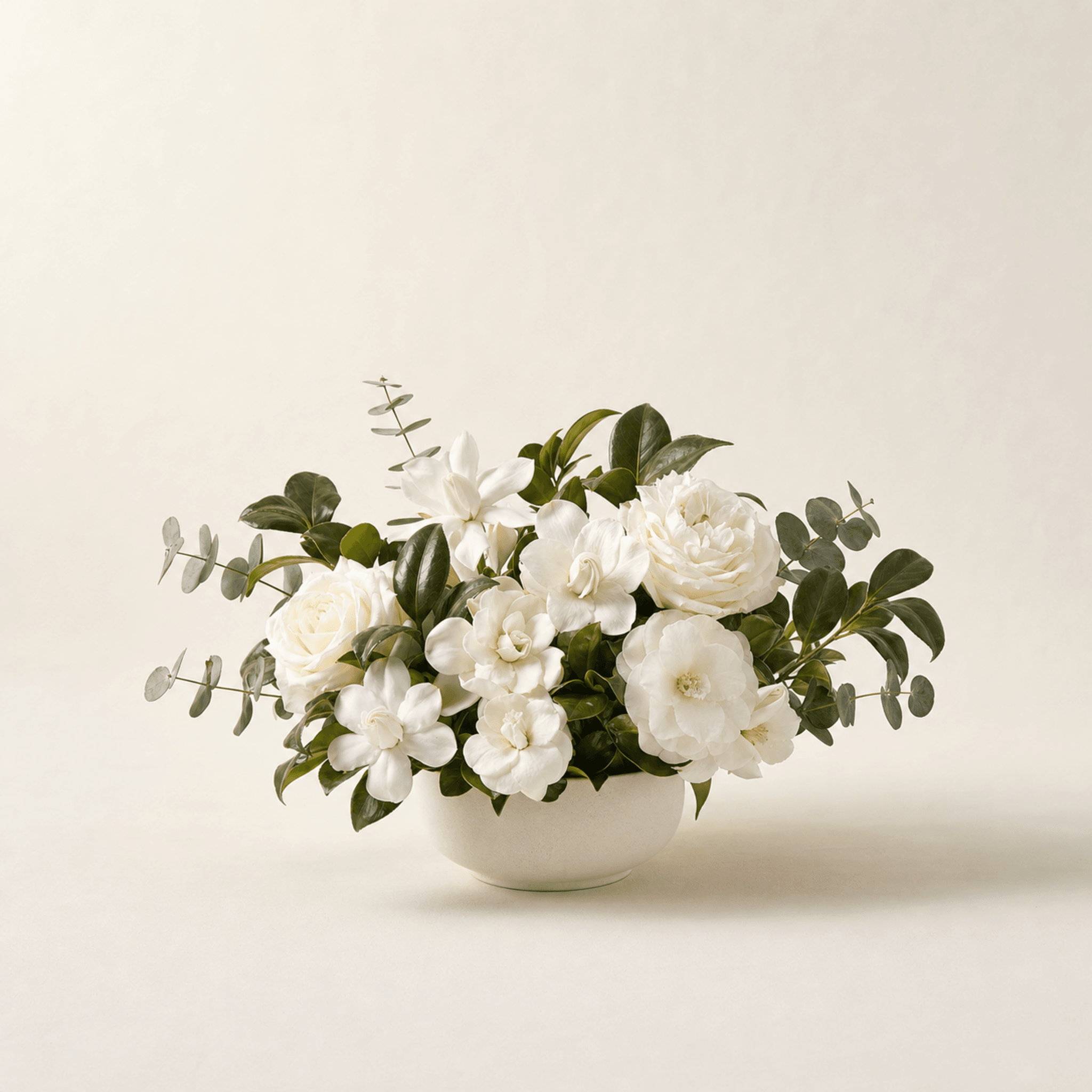 White gardenias, roses and camellias with eucalyptus in a white ceramic bowl