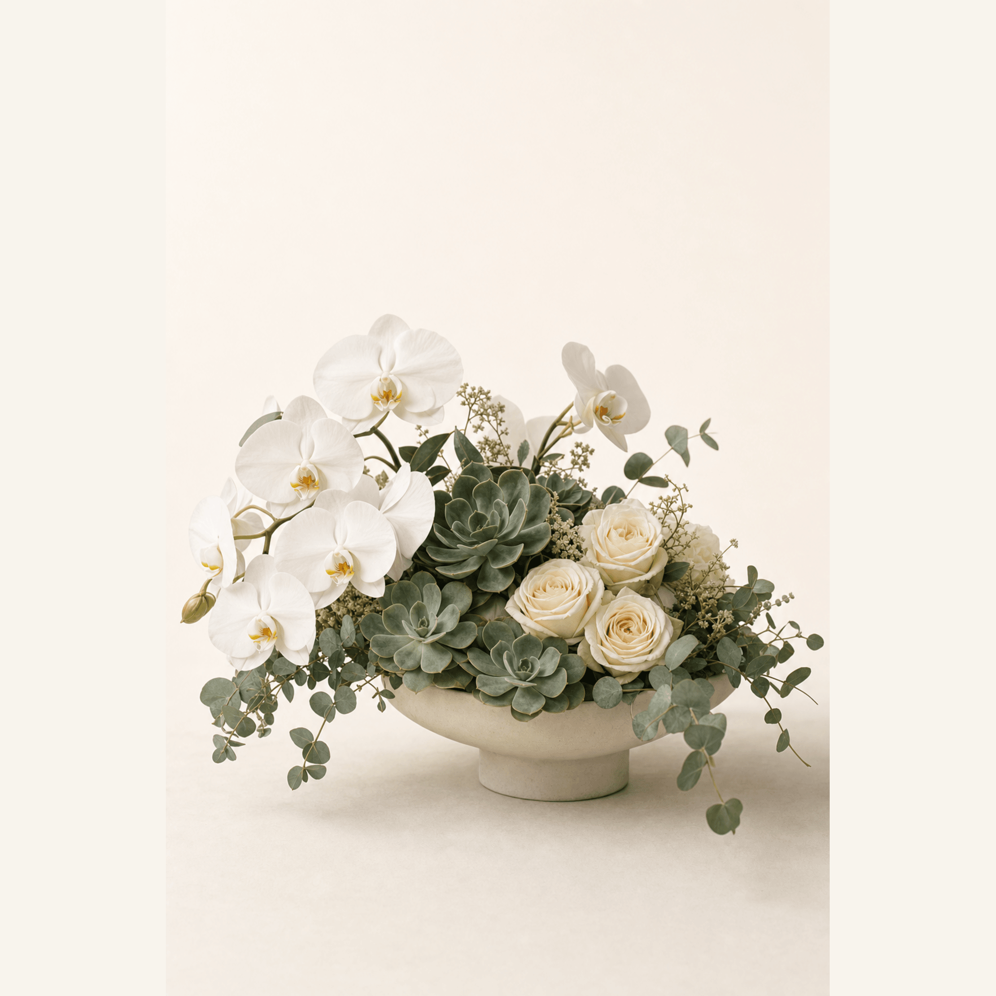 White phalaenopsis orchids, cream roses and grey-green succulents arranged in a shallow stone pedestal bowl