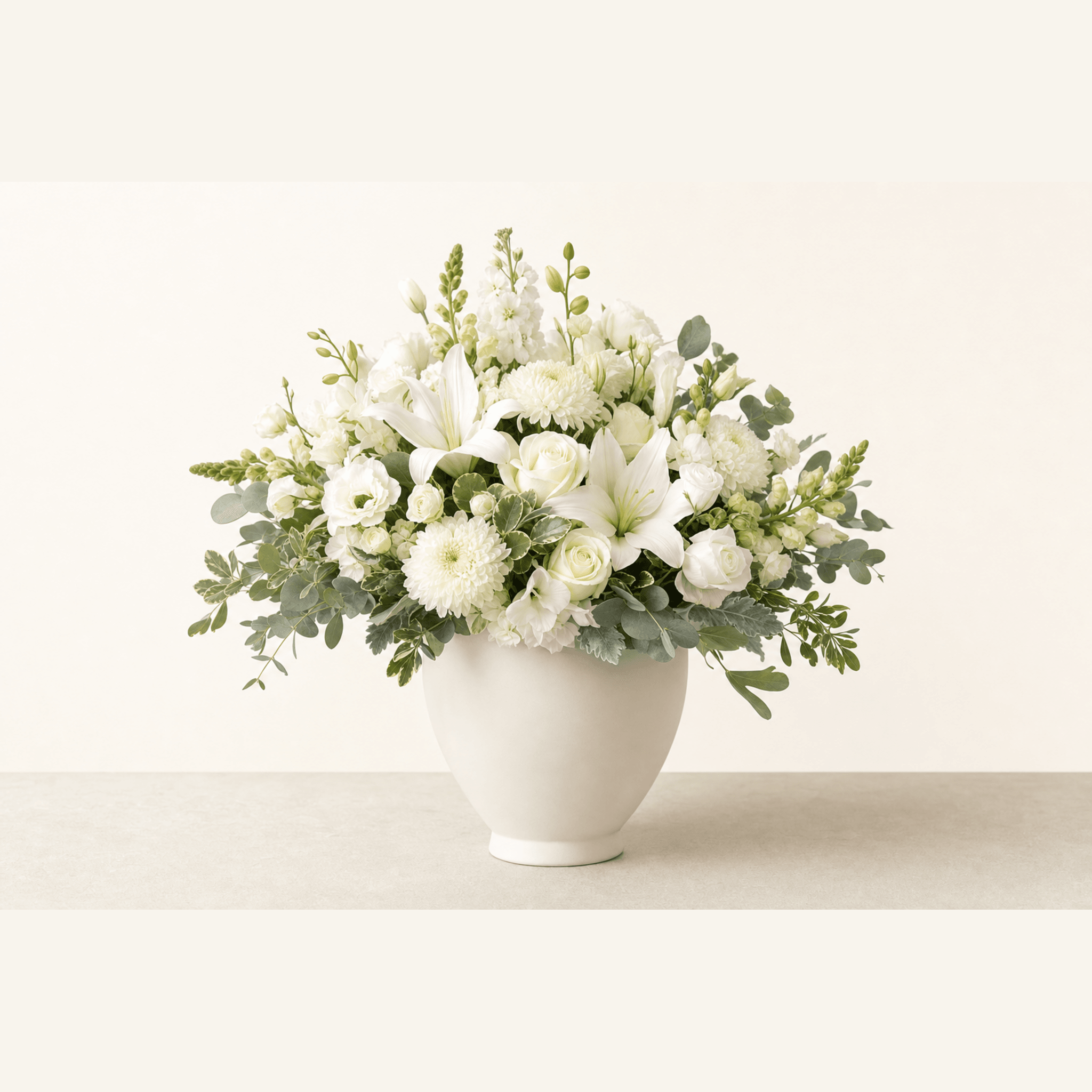 White lilies, roses, chrysanthemums and lisianthus with eucalyptus in a white ceramic bowl vase