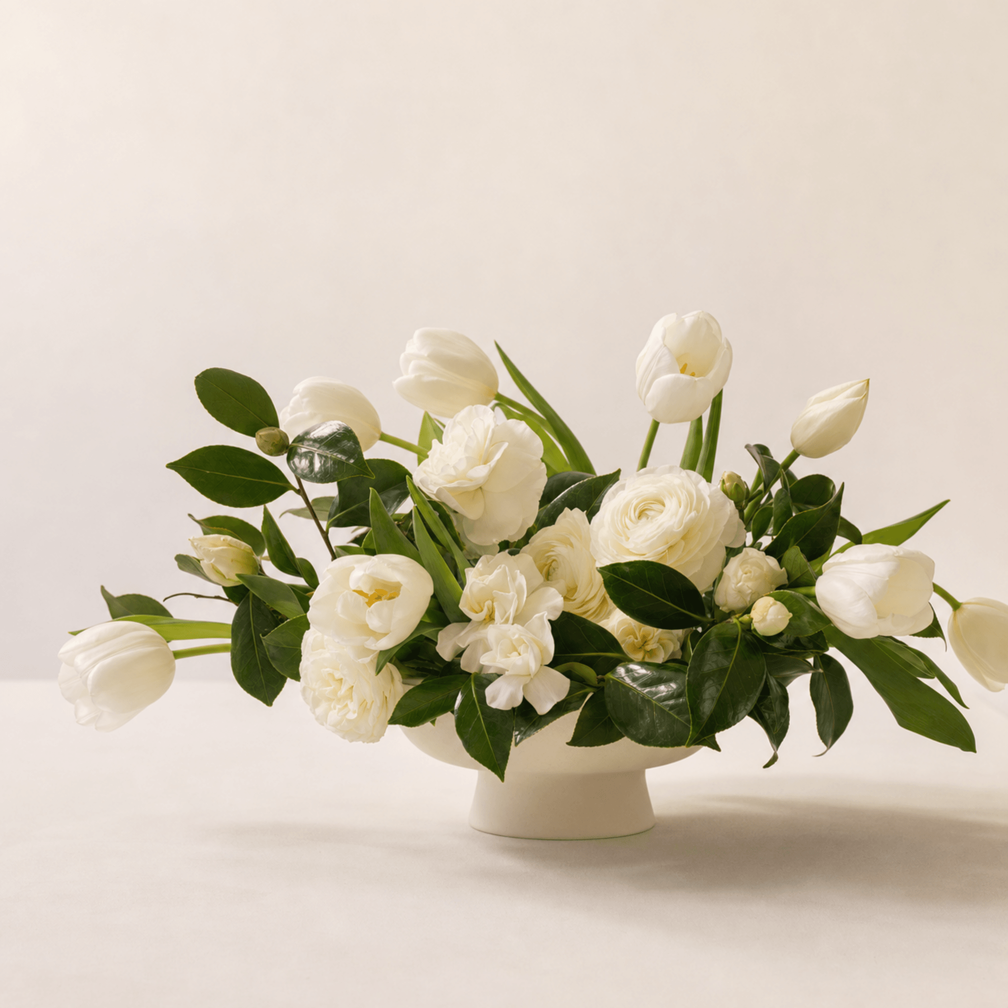 White tulips, ranunculus, garden roses and gardenias arranged in a white pedestal bowl